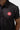 Close-up of the rubberized red Barra Shield logo on the chest of the black Red Shield Terra Mar polo, beside the collar and button placket.