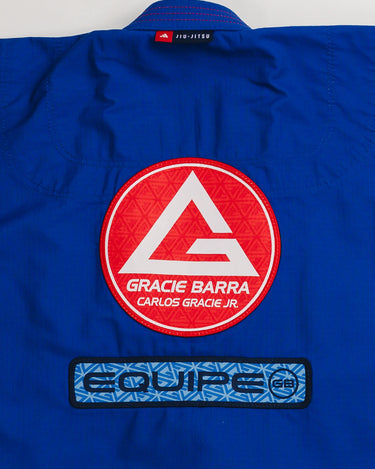 Close-up of back panel on blue Ripstop Lite Men’s BJJ kimono by adidas and Gracie Barra, showing large Red Shield patch above “Equipe GB” embroidery in blue.
