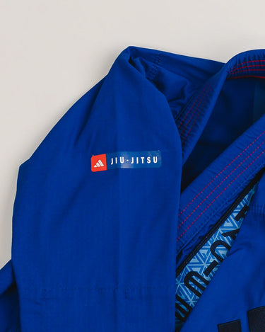 Shoulder detail of blue Ripstop Lite Men’s BJJ kimono by adidas and Gracie Barra, featuring “Jiu-Jitsu” patch, black adidas logo on sleeve, and front chest patch with Legacy G pattern in blue.