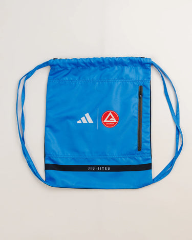 Blue drawstring kimono bag by adidas and Gracie Barra, featuring Red Shield patch, white adidas logo, black zipper pocket, and “Jiu-Jitsu” text detail.