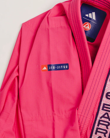Front upper detail of pink Ripstop Lite Women’s BJJ kimono by adidas and Gracie Barra, featuring “Jiu-Jitsu” patch, Red Shield chest patch, and “Gracie Barra” embroidered lapel trim.