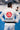 Back view of a practitioner wearing the white Ripstop Lightweight Kimono with a black belt on a blue gym mat, showing the large red circular Gracie Barra logo and navy Equipe patch across the back