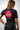 Back view of female model wearing Sakura V3 Women’s black BJJ rashguard with large red Gracie Barra shield logo and purple panel stitching, studio background