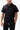 Stacked Button Up in Black — front view on model showing the short-sleeve button-up with chest pocket and curved hem, worn with black pants.