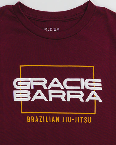 Close-up of puff print "Gracie Barra" logo in white with yellow "Brazilian Jiu-Jitsu" text on maroon fabric.
