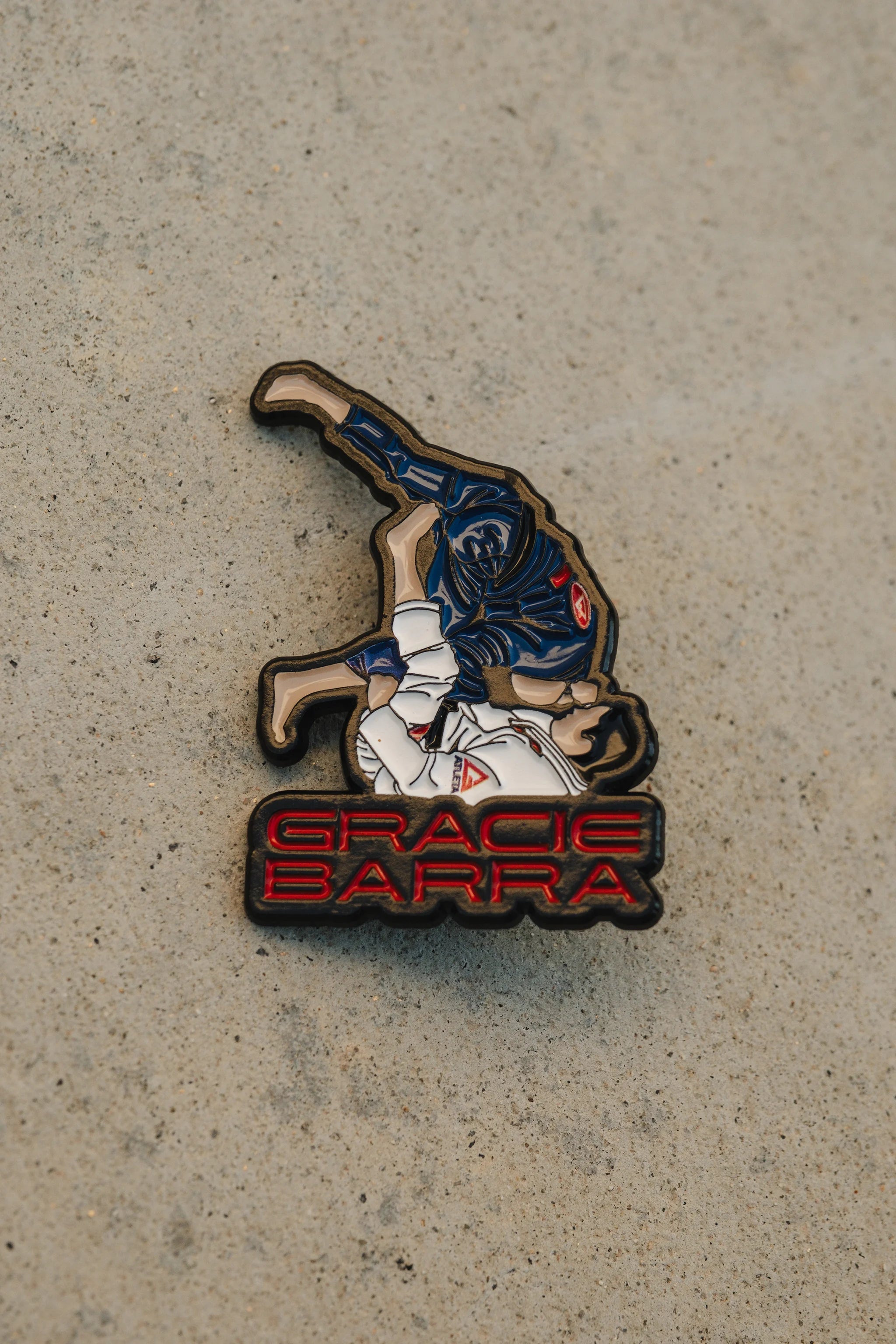 Close-up of the Gracie Barra sweep-position enamel pin on a concrete surface.