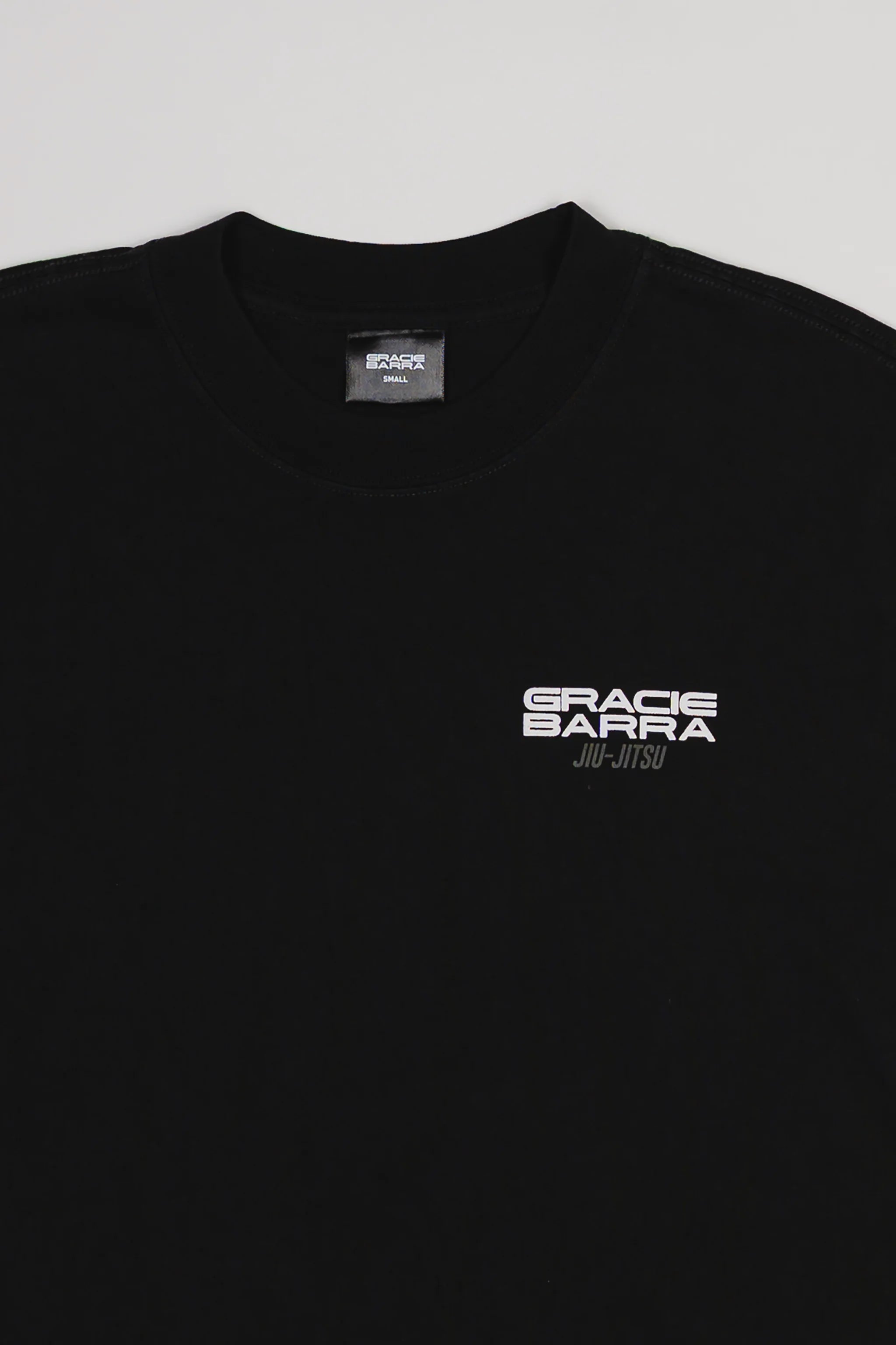 Close-up of chest area on Tactical Men’s Tee in black featuring white Gracie Barra Jiu-Jitsu logo, displayed on a light gray background.