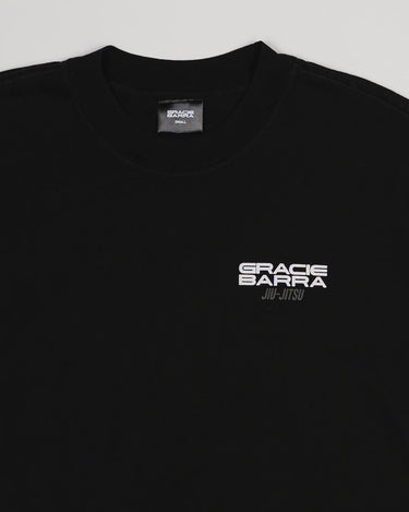 Close-up of chest area on Tactical Men’s Tee in black featuring white Gracie Barra Jiu-Jitsu logo, displayed on a light gray background.