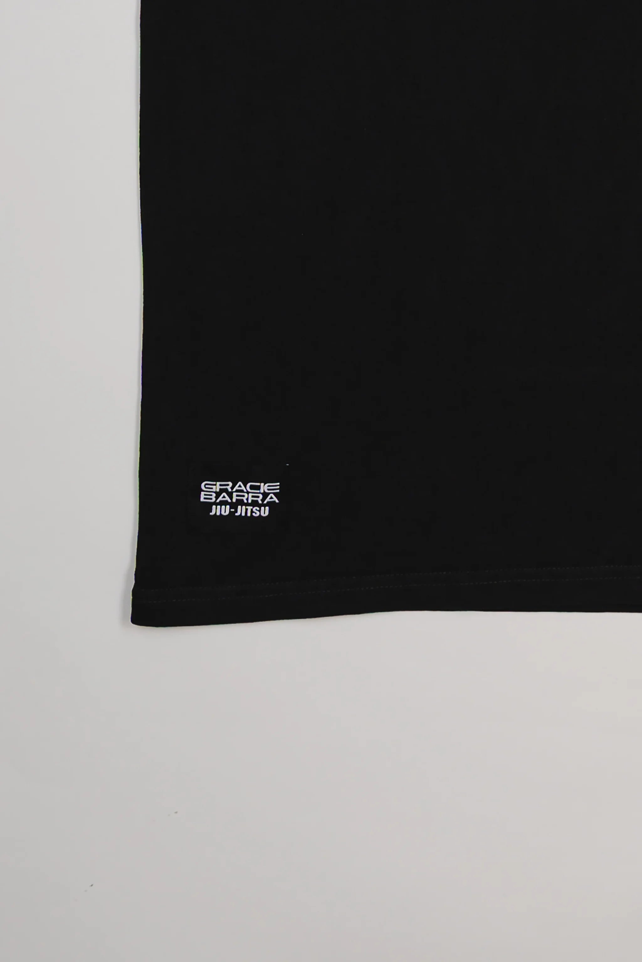 Close-up of hem on Tactical Men’s Tee in black with small rectangular Gracie Barra Jiu-Jitsu label, displayed on a light gray background.