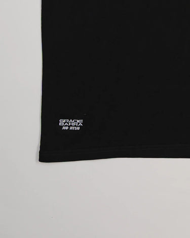 Close-up of hem on Tactical Men’s Tee in black with small rectangular Gracie Barra Jiu-Jitsu label, displayed on a light gray background.