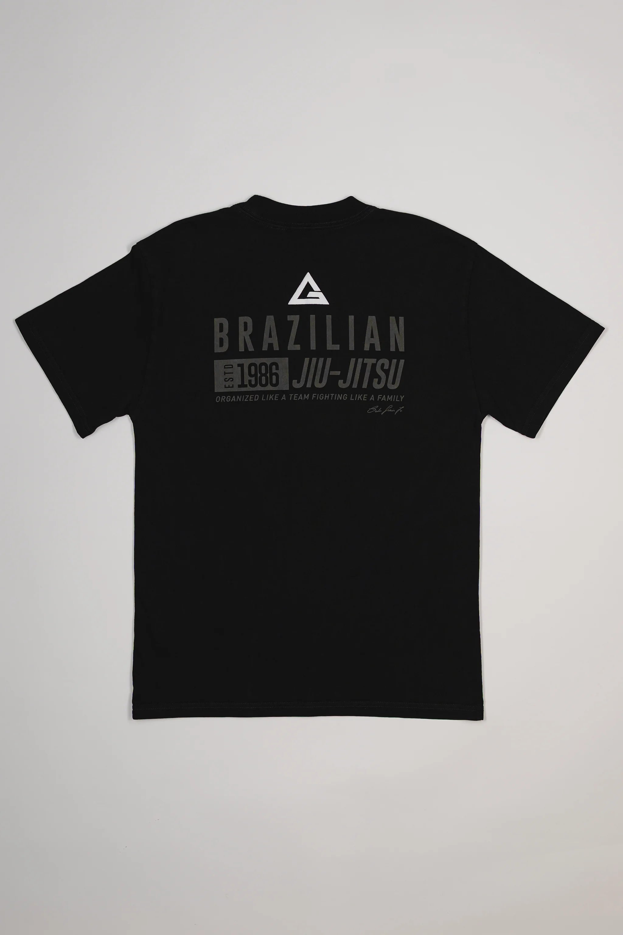 Back view of Tactical Men’s Tee in black featuring Legacy G logo and “Brazilian Jiu-Jitsu Est. 1986” text design in gray, displayed on a light gray background.