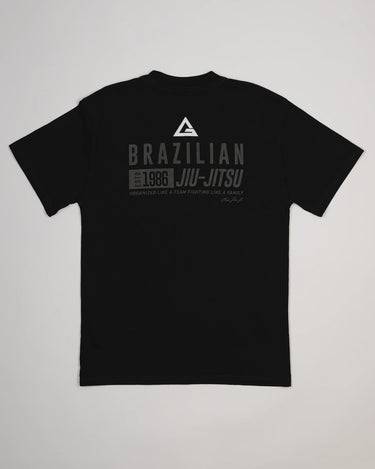 Back view of Tactical Men’s Tee in black featuring Legacy G logo and “Brazilian Jiu-Jitsu Est. 1986” text design in gray, displayed on a light gray background.