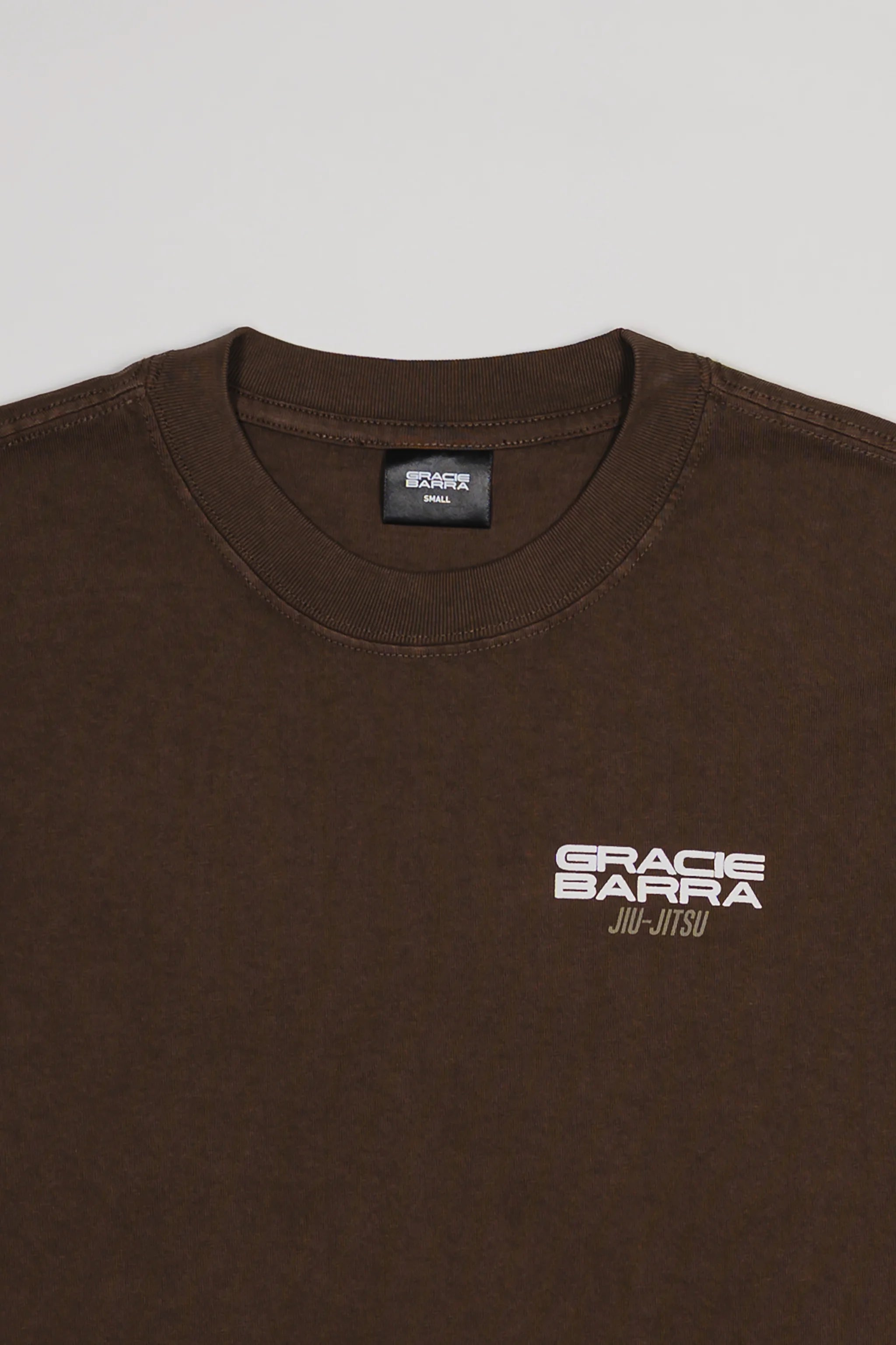 Close-up of chest area on Tactical Men’s Tee in dark brown with white Gracie Barra Jiu-Jitsu logo, displayed on a light gray background.