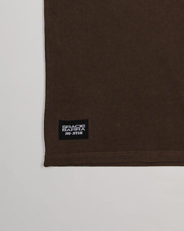 Close-up of bottom hem on Tactical Men’s Tee in dark brown with black woven Gracie Barra Jiu-Jitsu label, displayed on a light gray background.