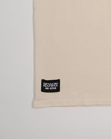 Close-up of bottom hem on Tactical Men’s Tee in natural beige featuring black woven Gracie Barra Jiu-Jitsu label, displayed on a light gray background.
