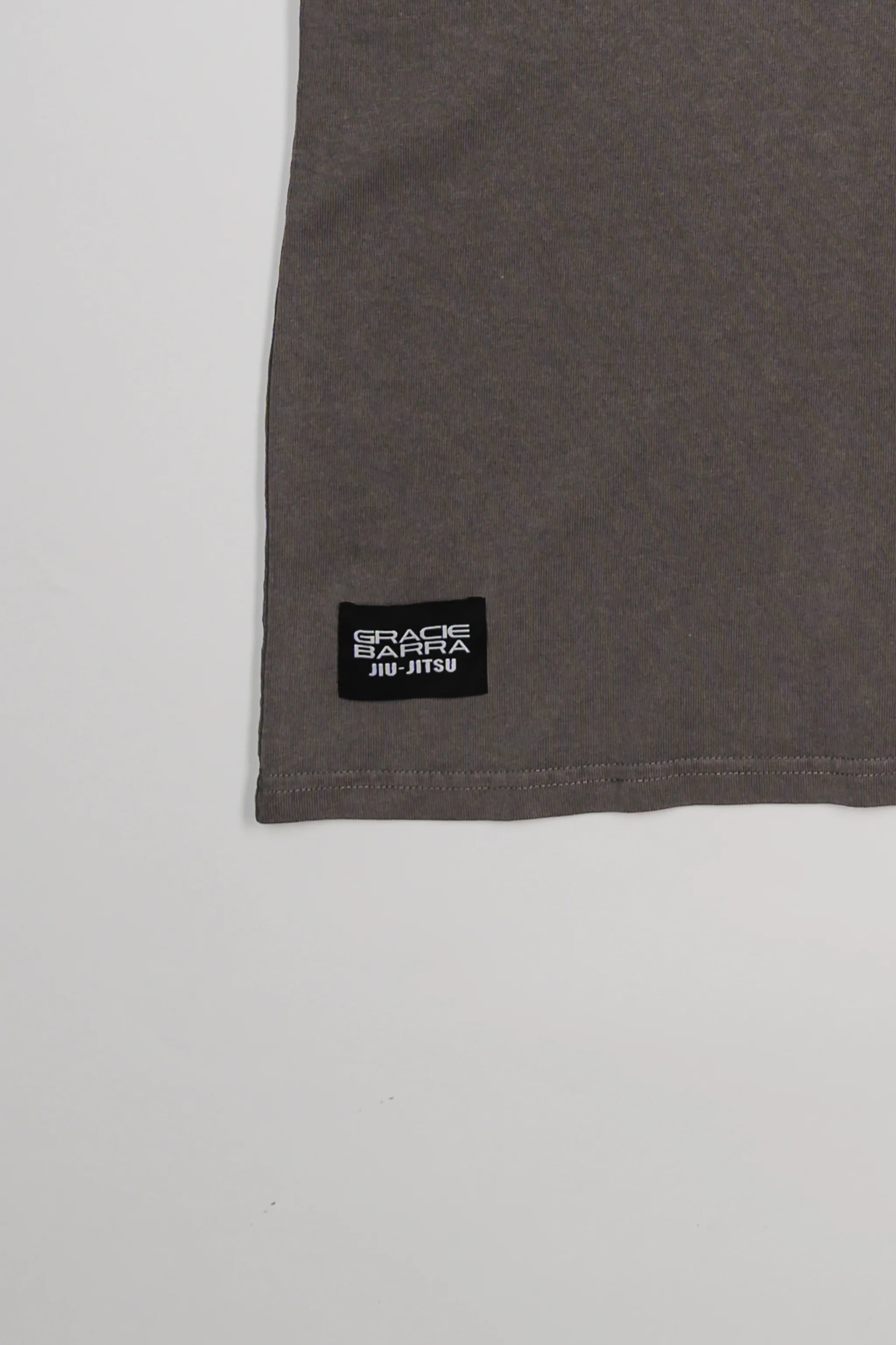 Close-up of lower hem on Tactical Women’s Tee in gray with black woven Gracie Barra Jiu-Jitsu label, displayed on a light gray background.