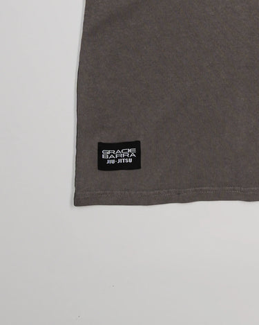 Close-up of lower hem on Tactical Women’s Tee in gray with black woven Gracie Barra Jiu-Jitsu label, displayed on a light gray background.