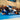 Two women in blue and white Gracie Barra competition kimonos in a match on the tournament mat in front of a seated crowd