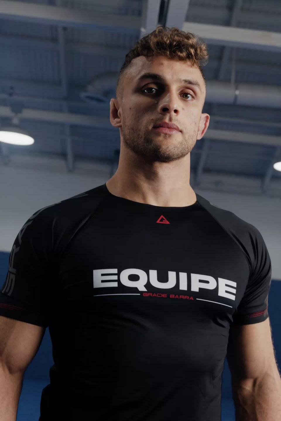 Two Gracie Barra athletes in black GB Essentials Techwear bow, drill, and roll on blue mats at a Gracie Barra School.