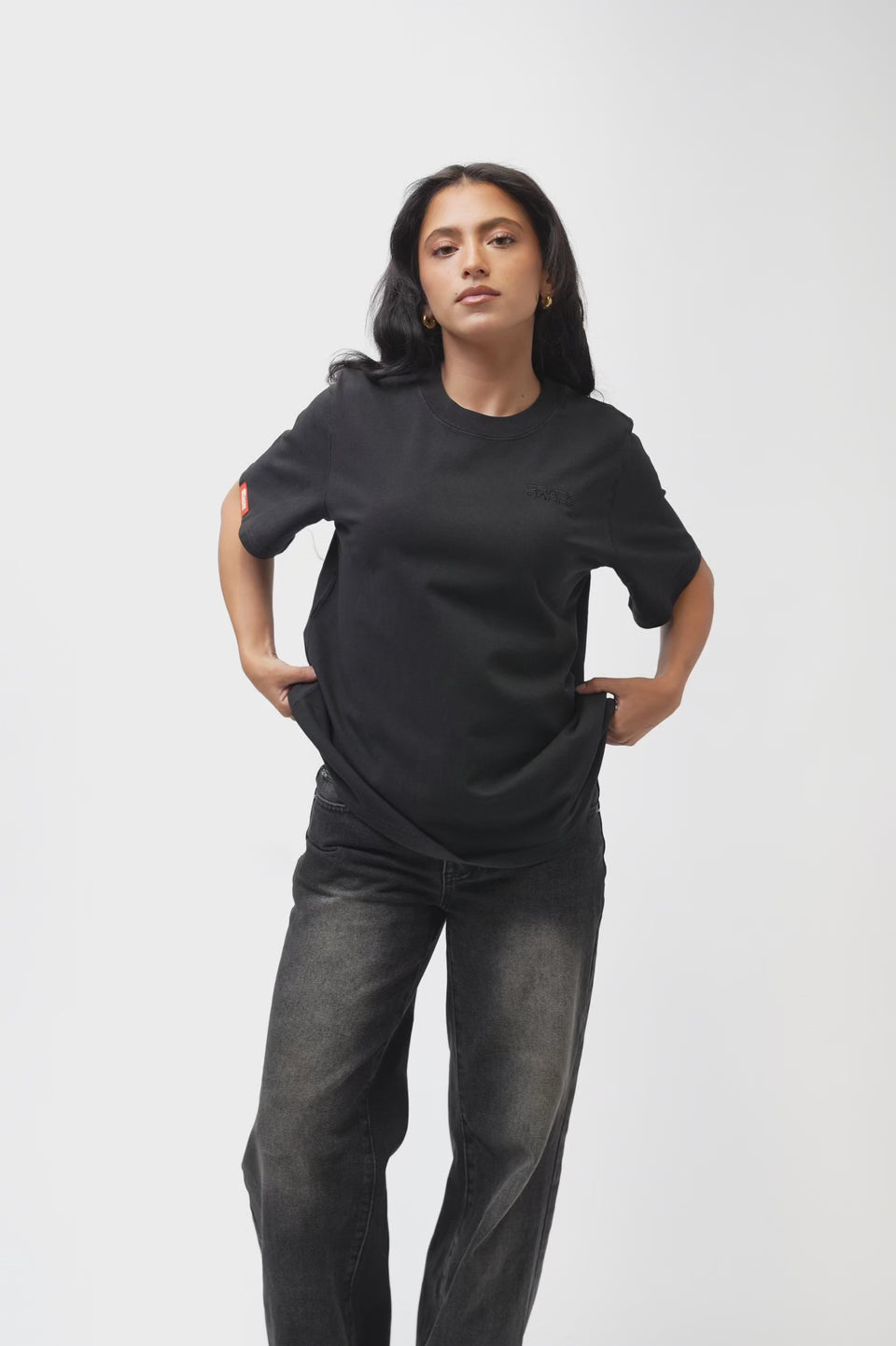 Emblem Womens Tee, black — 360° turnaround video showing the relaxed oversized fit front to back, with tonal Gracie Barra chest emblem, orange woven sleeve tag, and the Legacy G triangle logo above a "JIU-JITSU" graphic on the back.