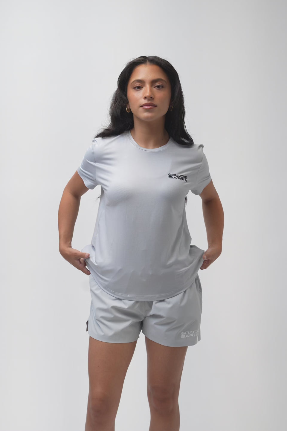 Video of a female model turning to show the front, back, and side of the Flow Women's Tech Tee in light grey and Frame Women's Short in light grey