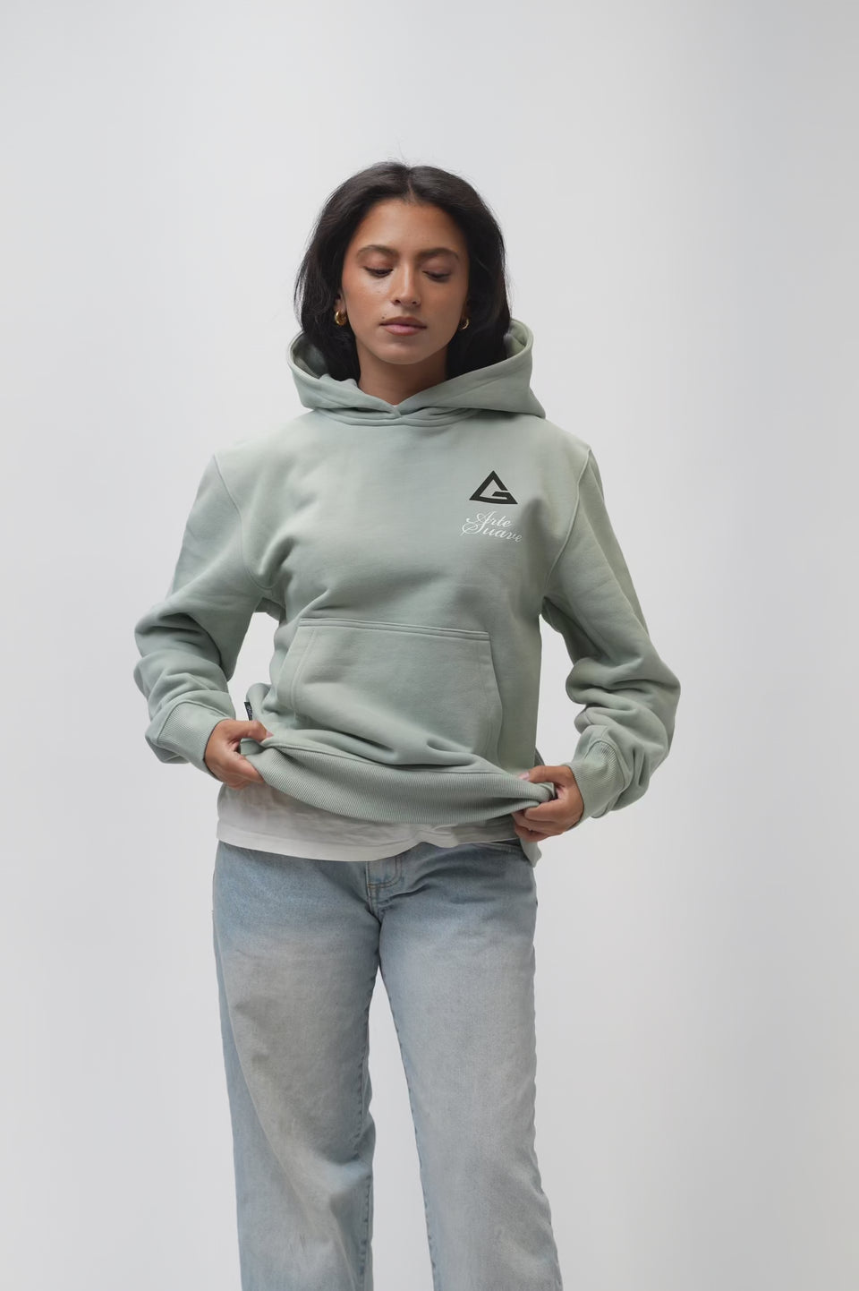 Video of the Arte Suave V3 Womens Hoodie in sage: model turns to show the Legacy G chest print and full-back 'Arte Suave' / 'Gracie Barra' graphic, then raises the hood.