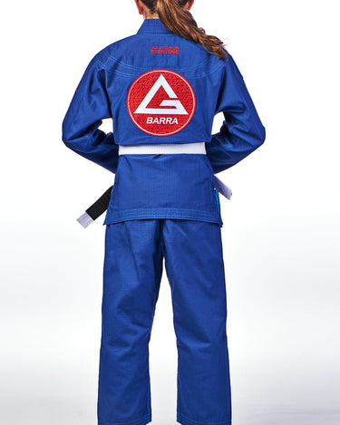 Back view of a child wearing the blue GBK Lite Ripstop kimono with a large Red Shield patch centered on the back, reinforced shoulder panels, clean stitching, and a tied white belt. Pants show a comfortable, reinforced fit.
