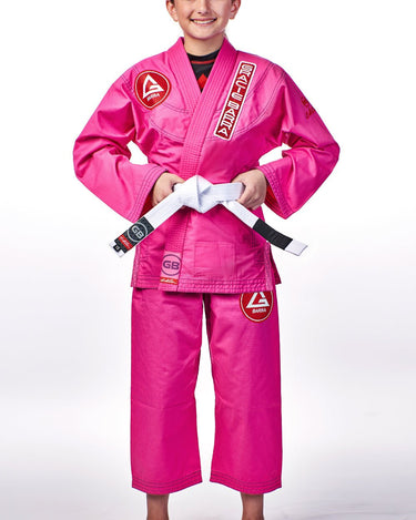 Young girl wearing the pink GBK Lite Ripstop kimono with Red Shield patches, a Gracie Barra lapel patch, and a GB label at the bottom of the jacket. The white belt is tied at the waist, showing a confident and comfortable fit for training.